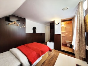 Une chambre à coucher avec un lit, une armoire, un miroir et une salle de bain visible à travers une porte ouverte.
