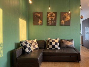A modern living room with a brown leather sofa, checkered cushions, and three wall-mounted artworks depicting jewelry. - Terrazza Gramsci – Spacious Private Terrace (Bologna)