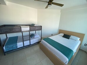 Ein Zimmer mit Etagenbetten und einem Einzelbett, einem Deckenventilator und Fliesenboden.