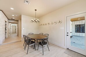 A dining area with a round table, six chairs, a chandelier, and wall-mounted decorative plates. - Iltis Hus on Lisbon | Historic 1853 Limestone Home (Castroville)