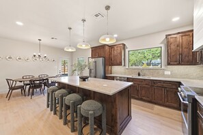 Een moderne keuken met een centraal eiland, barkrukken, houten kasten en een groot raam.