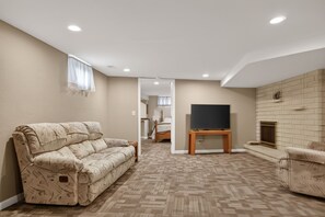 Uma sala de estar com sofá, televisão sobre um suporte, lareira e corredor que dá para um quarto.
