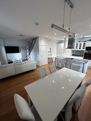 Una cocina moderna con armarios blancos, horno empotrado y comedor con mesa y sillas blancas.