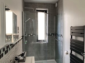 Un baño moderno con cabina de ducha de vidrio, un espejo grande y un toallero negro.