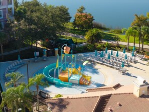 A water play area with slides and a fountain, surrounded by lounge chairs and umbrellas. - Your Orlando Retreat, 3BR at Prime Location (Orlando)