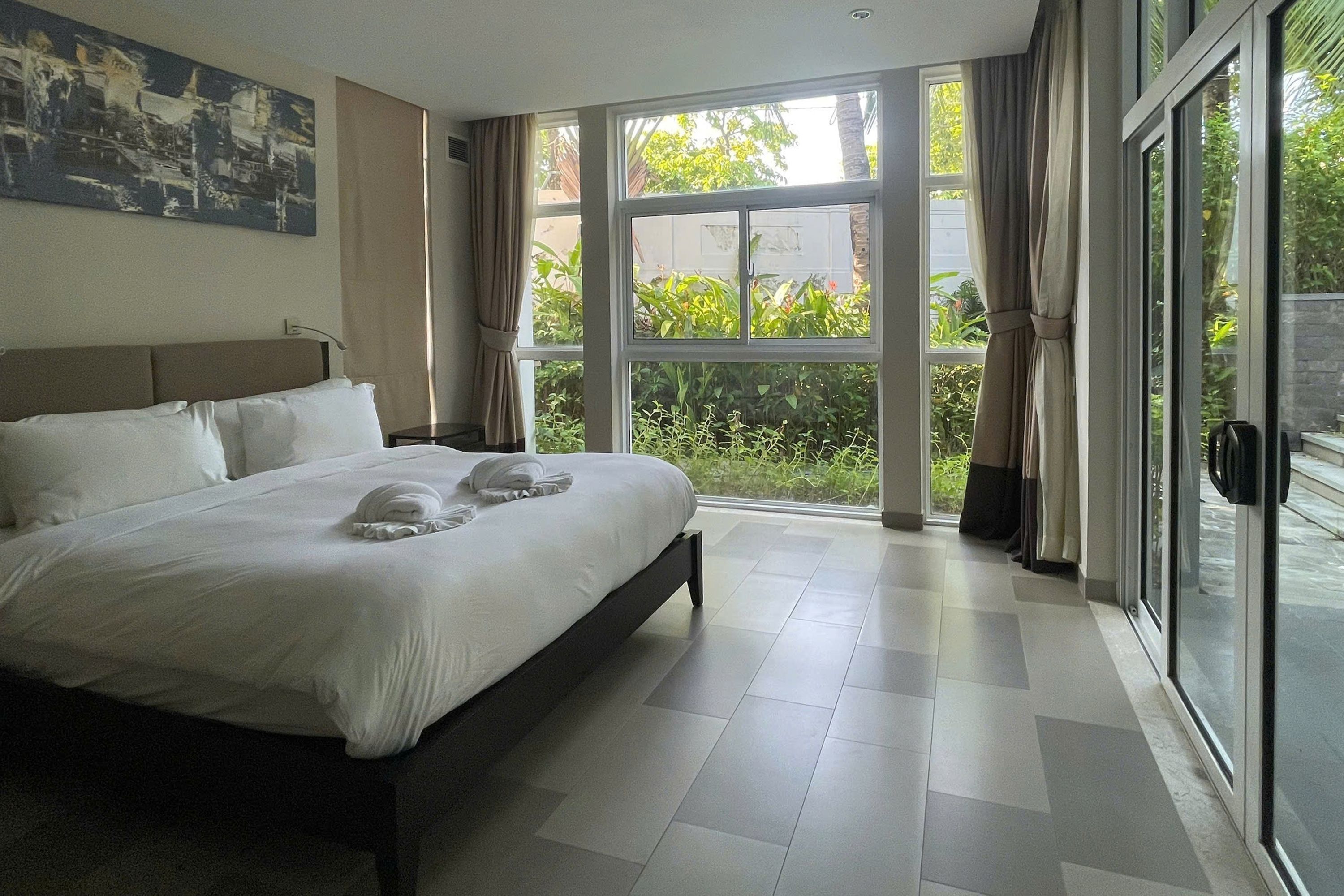 A hotel room with a large bed, a headboard, a painting on the wall, and a view through the glass doors.
