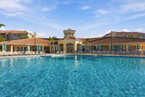 Een zwembad met ligbedden en parasols, omringd door gebouwen in mediterrane stijl.