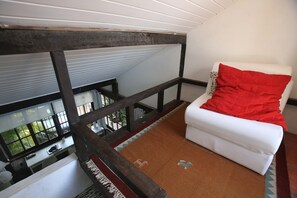 A balcony with a white sofa and red cushion, a wooden railing, and a view of greenery outside. - Casa Alto Astral em Buzios com Piscina (Búzios)