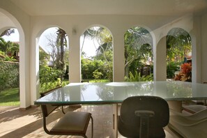 A glass-top table with chairs in a covered outdoor area with arches, surrounded by greenery. - Casa Alto Astral em Buzios com Piscina (Búzios)