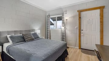 Ein Schlafzimmer mit Bett, Nachttisch, Lampe, Fenster mit Vorhängen und einer Tür.