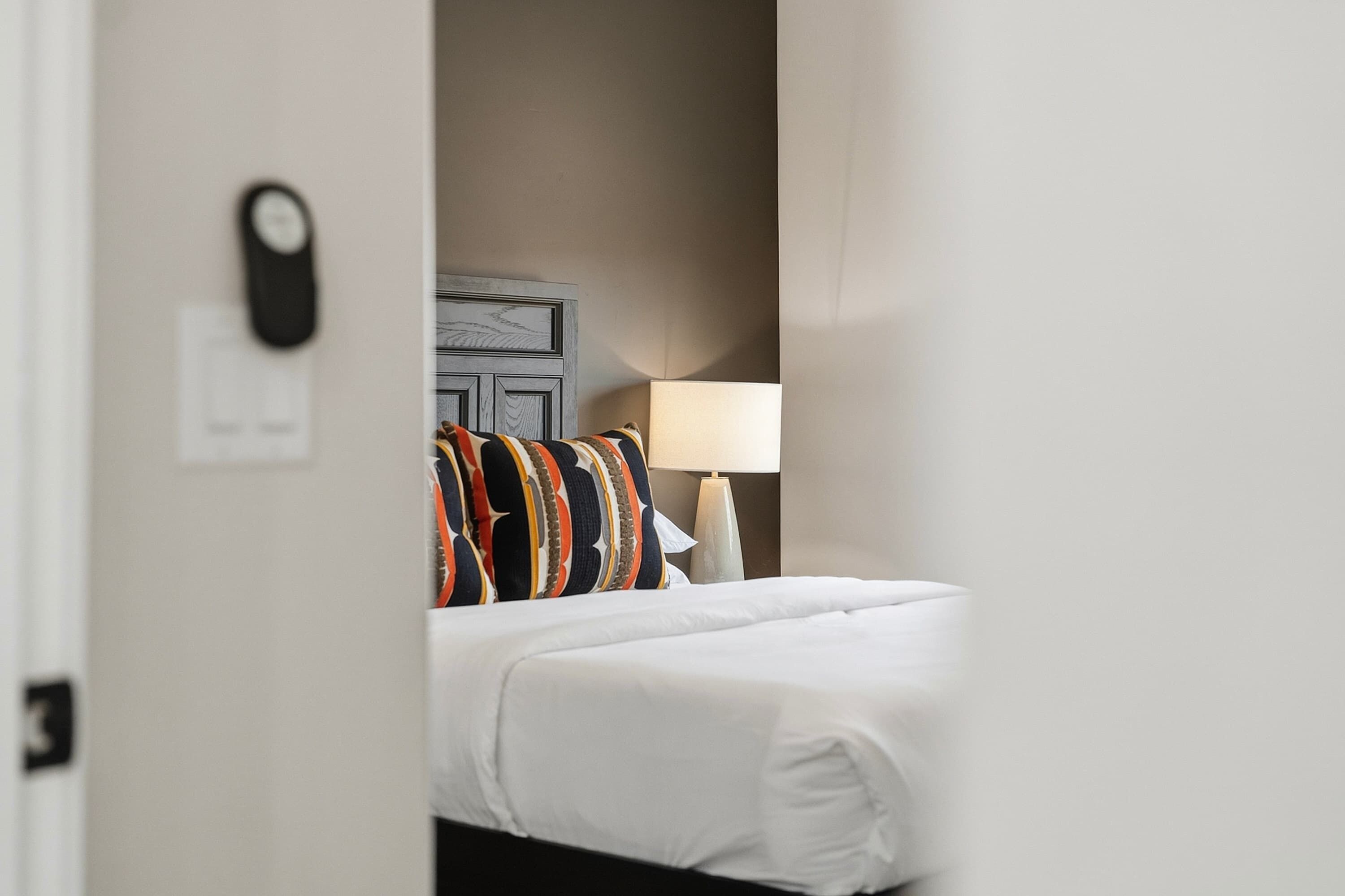 A hotel room with a bed, a nightstand, a lamp, and a wall-mounted clock.