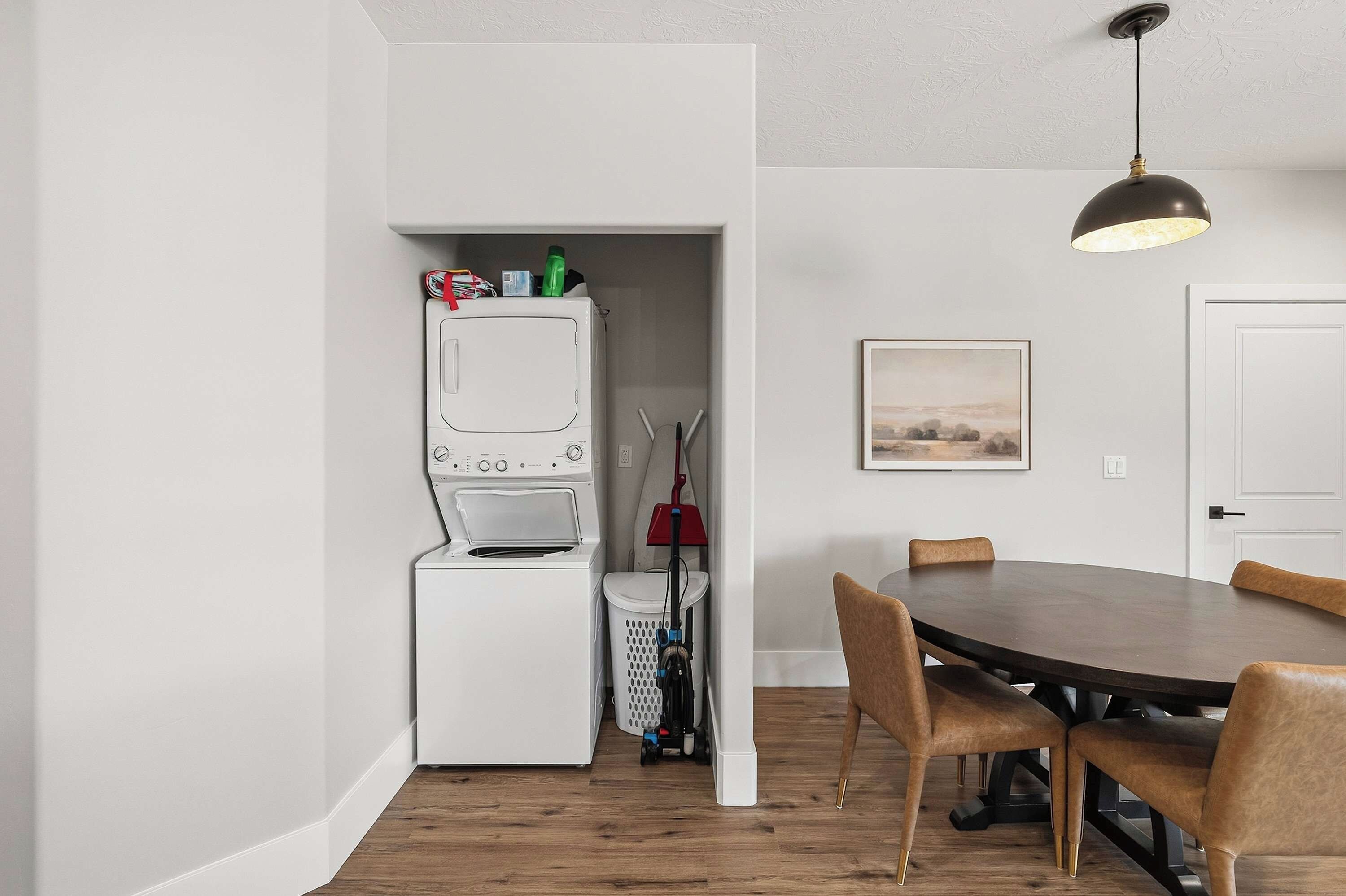 A compact kitchen with a built-in washer and dryer, a dining table with chairs, and a pendant light.