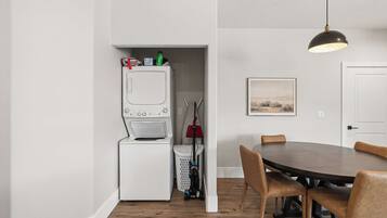 A compact kitchen with a built-in washer and dryer, a dining table with chairs, and a pendant light.