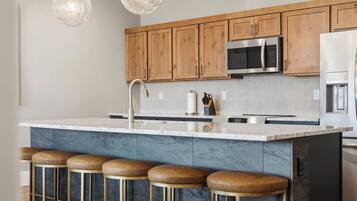 A modern kitchen with wooden cabinets, a stainless steel microwave, and a marble island with bar stools.