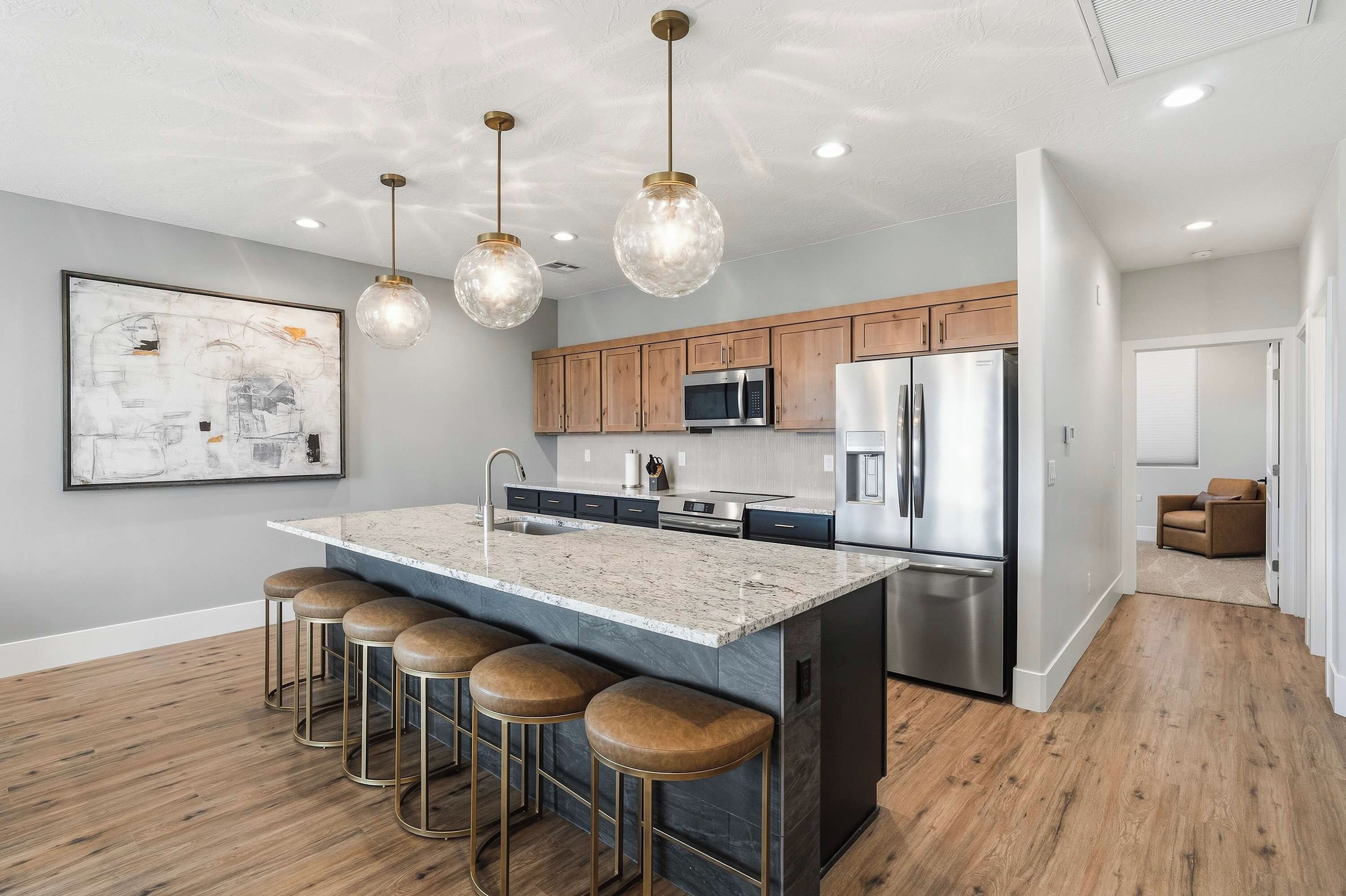 A modern kitchen with a central island, bar stools, stainless steel appliances, and pendant lighting.