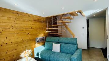 Una sala de estar moderna con una pared de madera, un sofá azul, una mesa blanca con un florero y una escalera de madera.