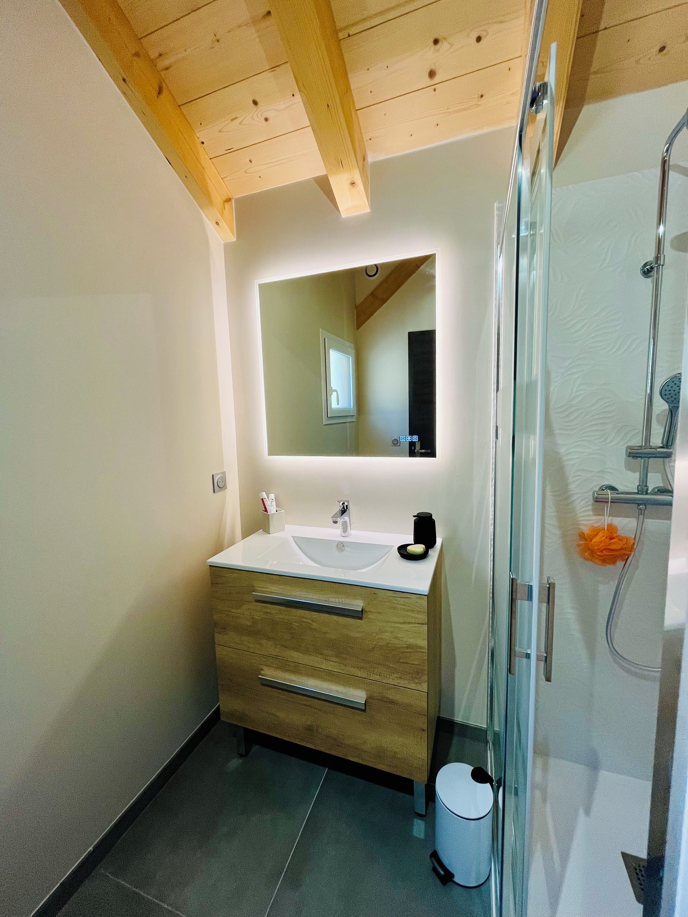 Un baño con techo de madera, un lavamanos con espejo y una zona de ducha.