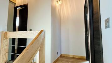 Un interior moderno con vigas de madera, una escalera y un pasillo que conduce a una puerta.