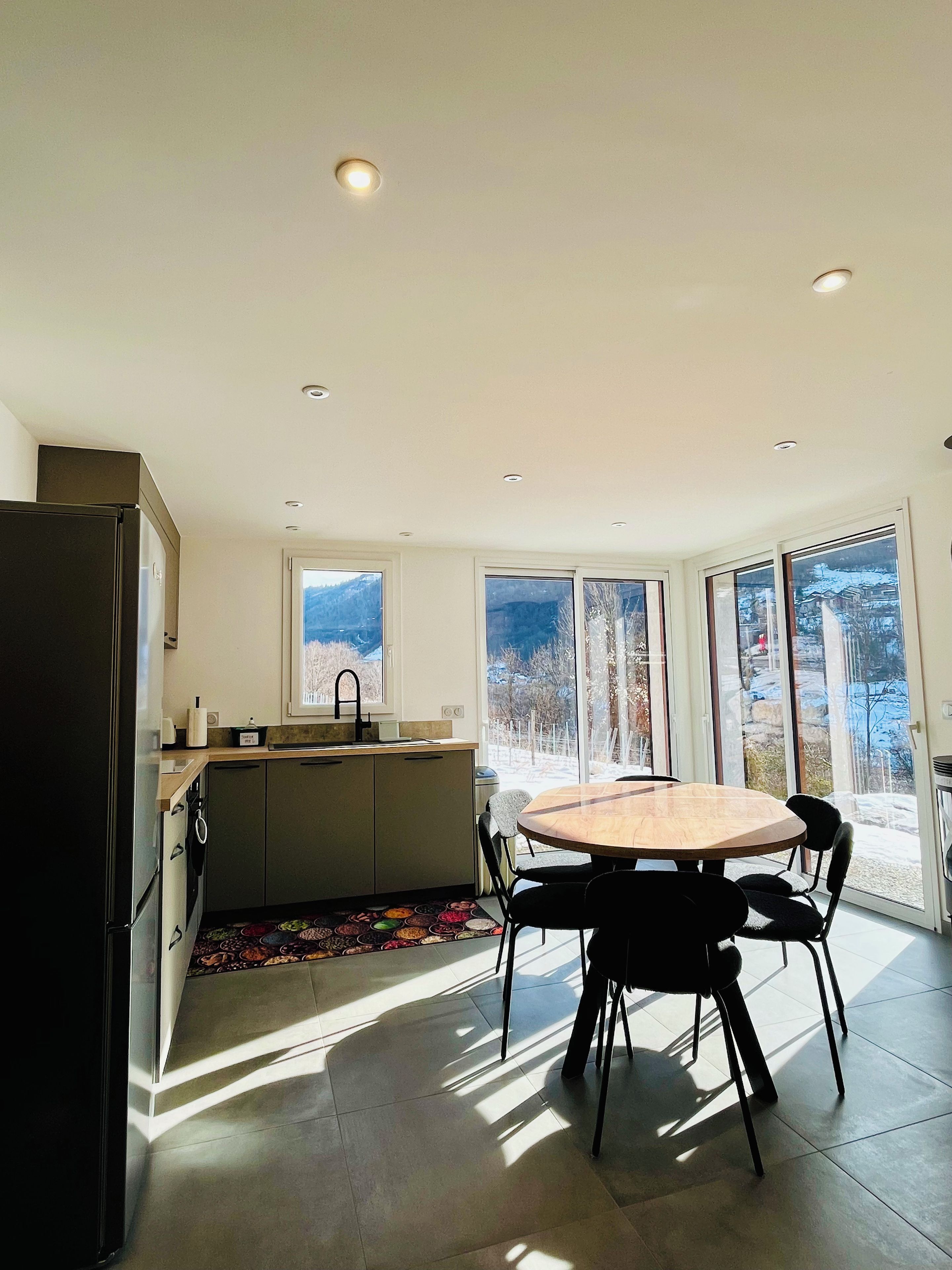 A modern kitchen with a dining area, large windows, and a view of the outdoors.