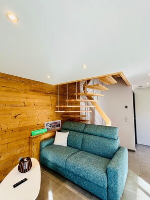 Ein modernes Wohnzimmer mit einer Holzwand, einem grünen Sofa, einem weißen Couchtisch und einer Holztreppe.