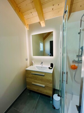 Ein modernes Badezimmer mit Holzboden, einem großen Spiegel, einem Waschbecken und einer Dusche.