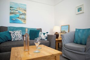 A living room with two sofas, a coffee table, and a lamp. There are paintings on the walls and a framed picture on the sideboard. - Trem Y Mor, New Quay (New Quay)