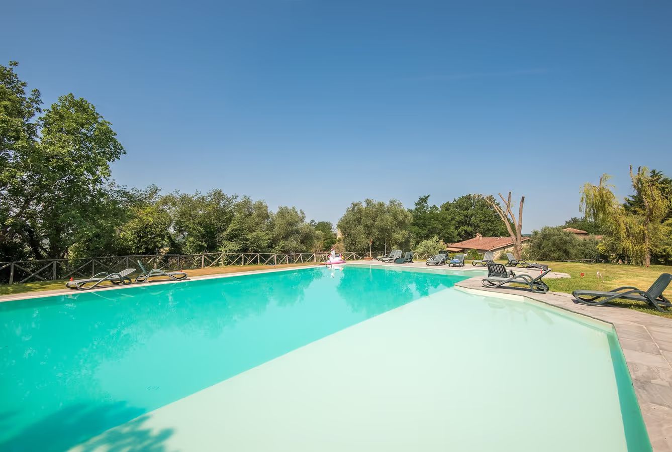 Ein rechteckiger Swimmingpool mit glasklarer, blauer Wasserfläche, umgeben von einer Umzäunung und Bäumen.