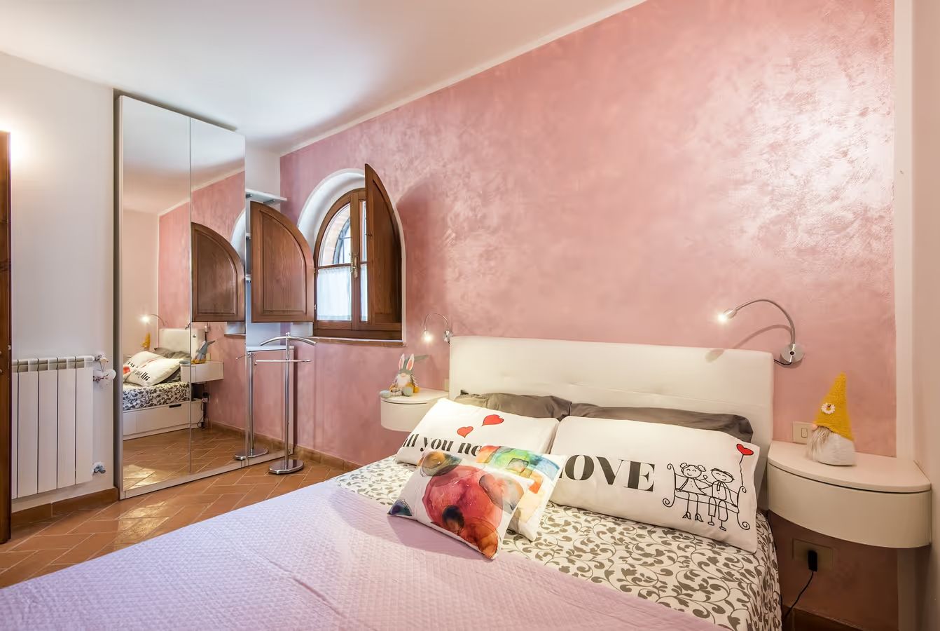 Ein Schlafzimmer mit einem Bett, einem Nachttisch, einem Spiegel und einem Fenster.