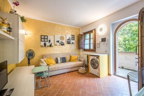 Ein kompakter Wohnraum mit einer Couch, einer Waschmaschine, einem Ventilator und Kunstwerken an der Wand.