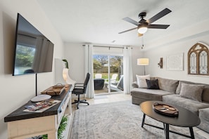 Ein modernes Wohnzimmer mit Flachbildfernseher, Deckenventilator, Sofa, Couchtisch und einer Schiebetür zu einer Außenpatio.