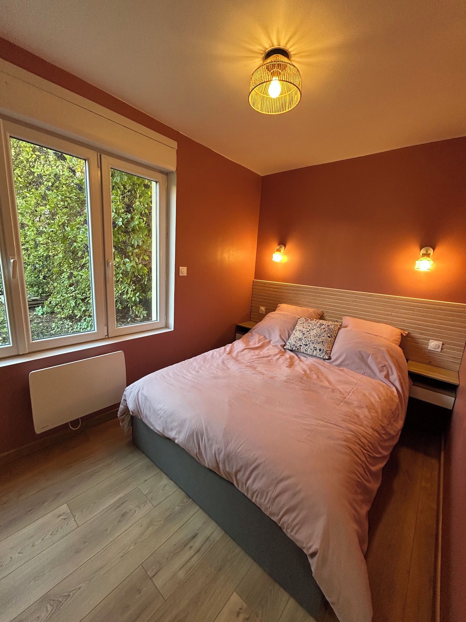 Un dormitorio con una cama, dos lámparas de noche, una ventana y un radiador.