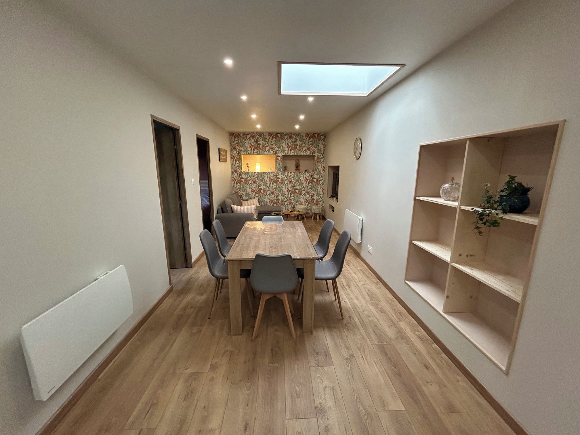 Een eetgedeelte met een houten tafel en stoelen, een dakraam en een decoratieve wand met een klok.