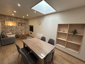 Una sala de estar moderna con una mesa de comedor, sofás, un televisor y un muro decorativo.