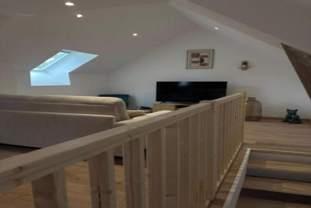 Een moderne loftkamer met schuine plafonds, een ingebouwde televisie, een bank en een houten leuning.