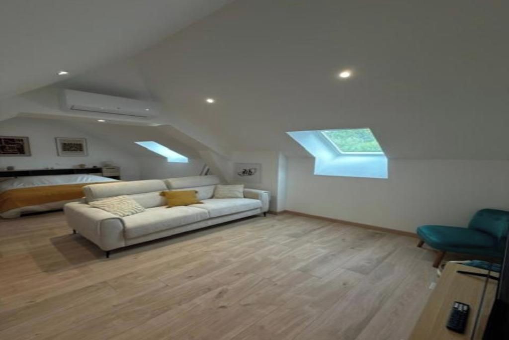 A spacious loft with a high ceiling, a white sofa, a teal chair, and a skylight.