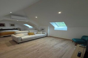 A spacious loft with a high ceiling, a white sofa, a teal chair, and a skylight.