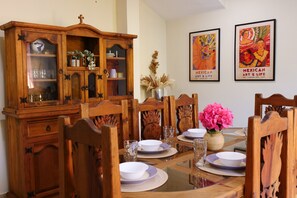 A dining area with a wooden table set for four, surrounded by chairs with carved backs. A wooden cabinet with glass doors is to the left. - Beautiful 5-bedroom house with pool in Historic Centro Merida - Casa Abogado (Merida)