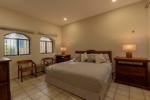 A bedroom with a large bed, two bedside tables, a chair, and two windows with decorative iron bars. - Beautiful 5-bedroom house with pool in Historic Centro Merida - Casa Abogado (Merida)