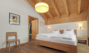 A bedroom with a wooden bed, a chair, and a door leading to another room. - MATTERHORN VIEW RETREAT – ELEGANT 4-BEDROOM ZERMATT APARTMENT (Zermatt)
