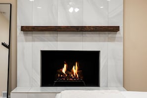 Une cheminée au design moderne, dotée d’un manteau de couleur blanche et d’une étagère en bois située au-dessus.