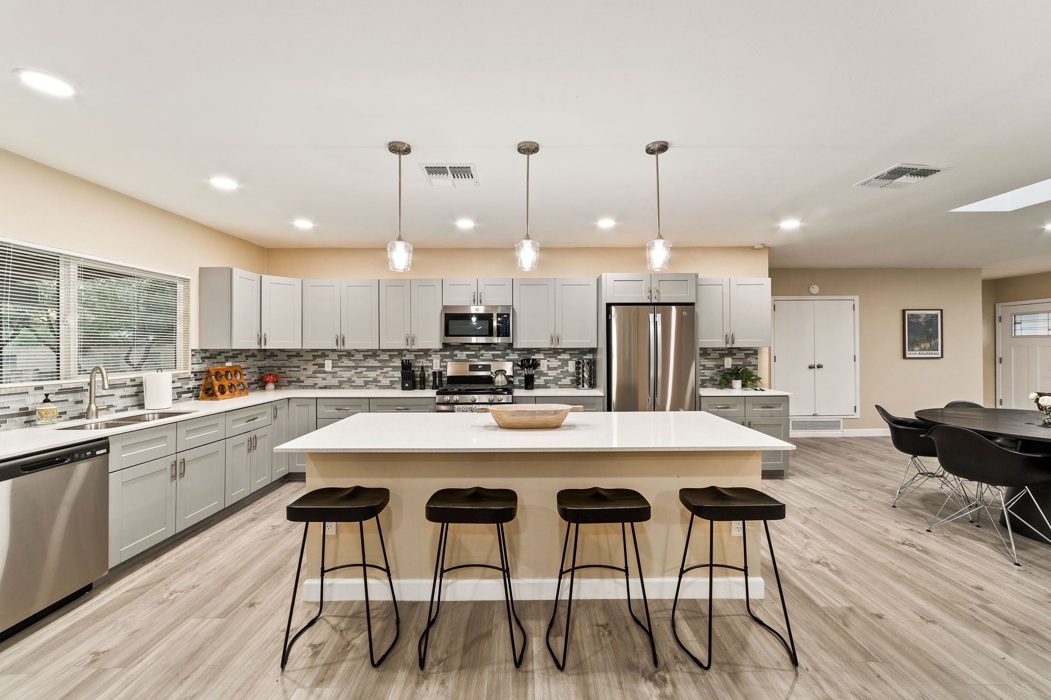 Una cocina moderna con una isla central, taburetes de bar, electrodomésticos de acero inoxidable e iluminación colgante.