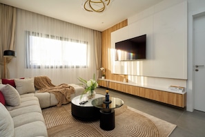 A modern living room with a sofa, a coffee table, a TV mounted on the wall, and a large window with curtains. - Premium one-bedroom apartment in Fann-Mermoz · Corniche within walking distance (Dakar)