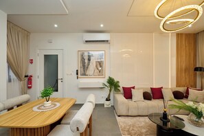 A modern living room with a wooden dining table, a sofa set, a coffee table, and a large painting on the wall. - Premium one-bedroom apartment in Fann-Mermoz · Corniche within walking distance (Dakar)