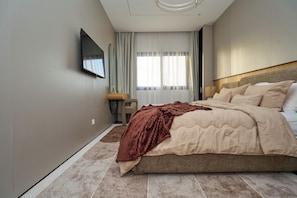 A hotel room with a large bed, a flat-screen TV mounted on the wall, a bedside table with a lamp, and a window with curtains. - Premium one-bedroom apartment in Fann-Mermoz · Corniche within walking distance (Dakar)