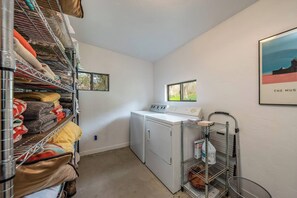A laundry room with a washing machine, drying rack, and shelves with folded towels. - Private! Hidden Gem on the River! (Three Rivers)