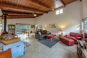 A spacious living room with a high ceiling, a fireplace, a dining area, and a cozy seating area with a red sofa and ottoman. - Private! Hidden Gem on the River! (Three Rivers)