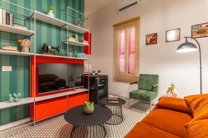 Una sala de estar con mueble de entretenimiento rojo, sillón verde y sofá naranja.
