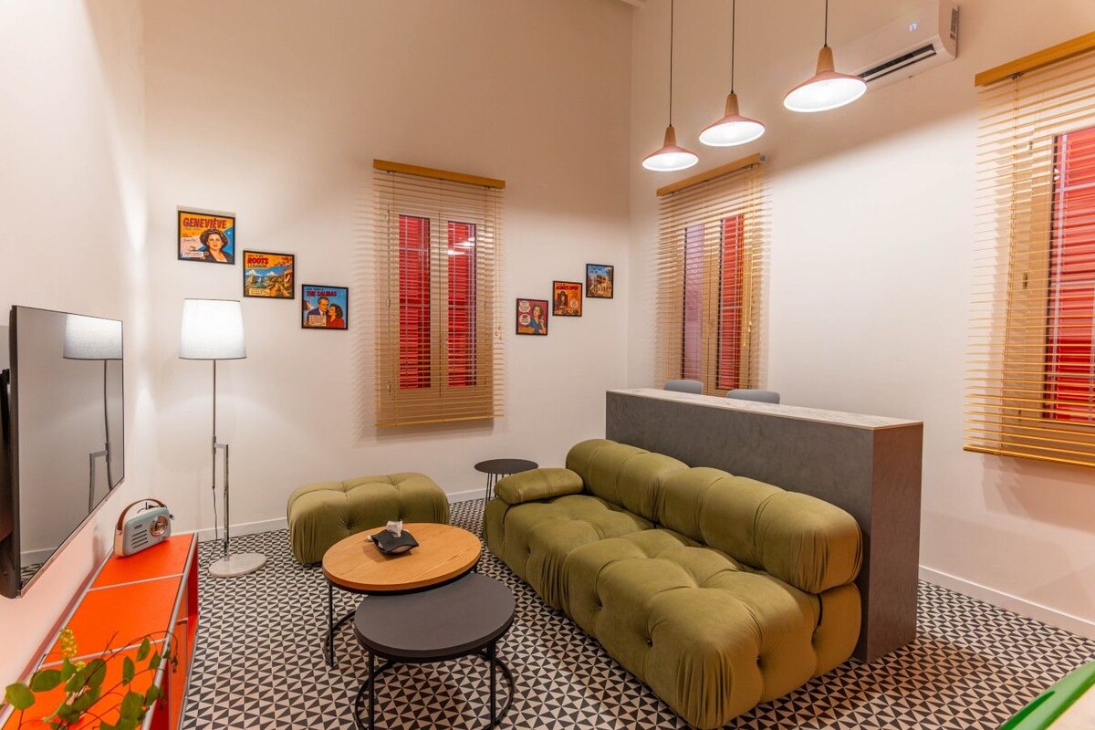 Una sala de estar moderna con un sofá, dos sillones, una mesa de centro, un televisor de pantalla plana y una mesita de noche con una lámpara.
