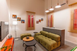 Una sala de estar moderna con un sofá, dos sillones, una mesa de centro, un televisor de pantalla plana y una mesita de noche con una lámpara.