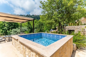 Piscina rectangular a l'aire lliure amb un marc de pedra, envoltada de verdura i una paret de pedra.